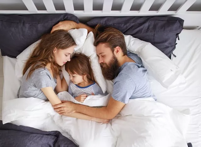 Familie schläft zusammengekuschelt im Bett